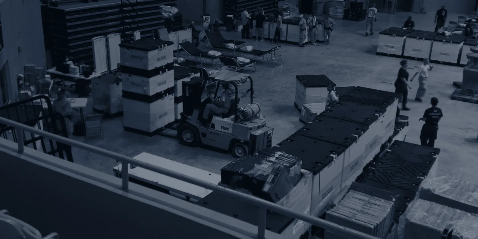 Warehouse floor seen from a mezzanine, people and stock spread across separate stations